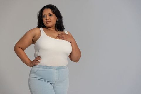 Confident plus-size woman wearing white tank and light blue jeans mid-30s studio portrait