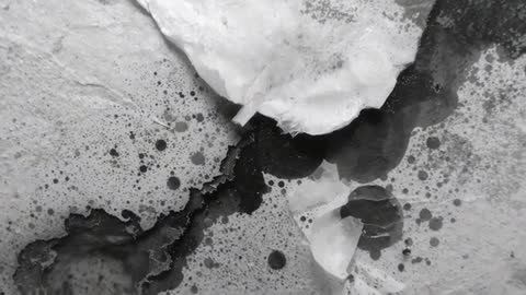 Macro video revealing torn white layer peeling from textured wall with dark ink stains