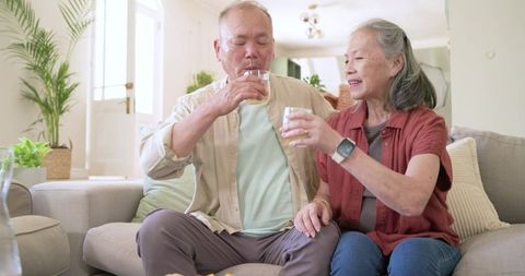 Senior couple sharing hydration moment on cozy sofa, healthy aging and companionship