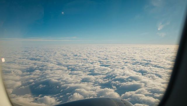 Revealing rolling cloud deck from airplane window with engine and sunlit horizon above clouds