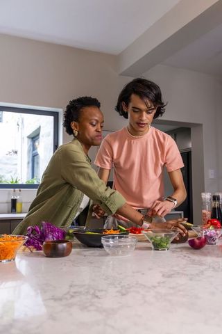 African american woman and asian man chopping vegetables together at marble kitchen island