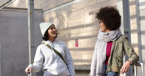 Two friends walking and chatting with rolling luggage along sunlit urban walkway