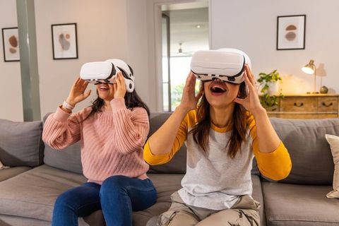Friends enjoying virtual reality at home laughing while wearing white vr headsets