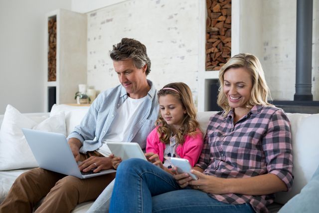 Family using laptop, digital tablet and mobile phone in living room at home