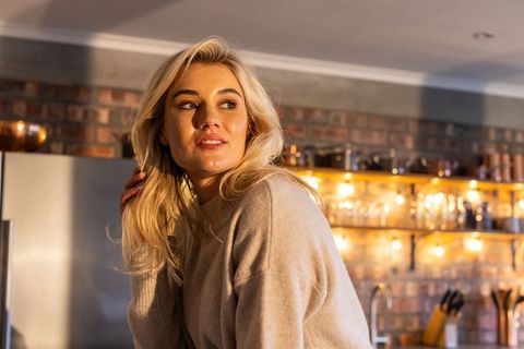 Blonde woman leaning on kitchen counter wearing cozy knit sweater in warm amber light