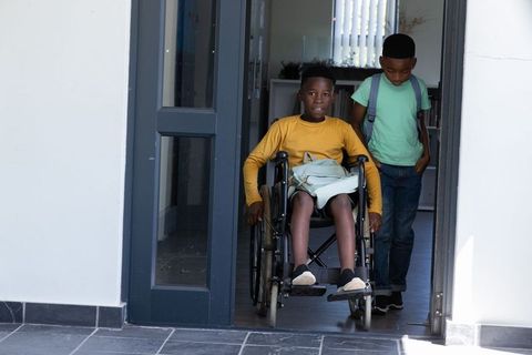 Young african american student entering school in wheelchair with supportive friend and backpacks