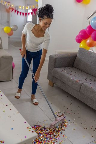 Teen sweeping confetti after party in modern living room with balloons and banner