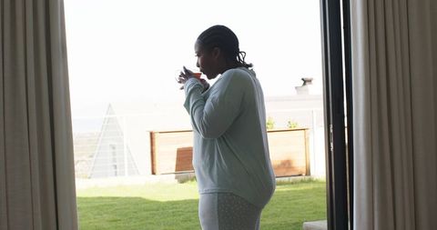 African american woman enjoying morning tea by open patio door in cozy loungewear