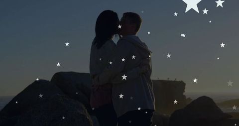Kissing couple embracing on rocky shore at dusk with star overlay and coastal silhouette