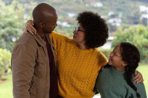 Diverse family embracing on covered porch, parents and child sharing warm moment