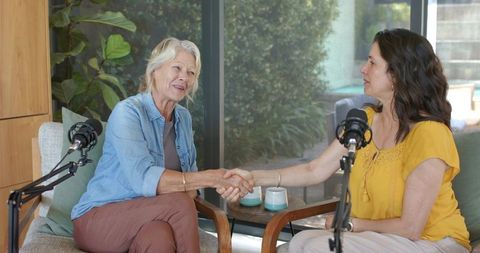 Mature women hosting podcast shaking hands during interview in cozy home studio
