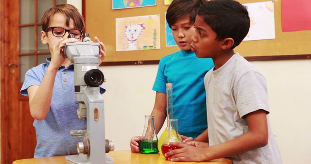 Schoolchildren engaged in a science experiment, with one looking through a microscope while the others hold flasks with colorful liquid. Ideal for use in educational materials, science programs for children, and advertisements promoting educational products and curiosity-driven learning.