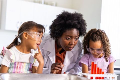 Stem mentor guiding young girls through colorful chemistry experiment with safety goggles