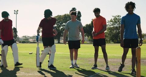 Diverse male teammates walking onto cricket pitch preparing for practice and crease drill