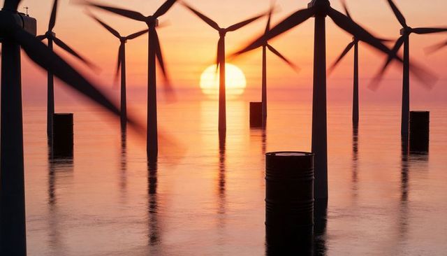 Glowing sunset illuminating offshore wind turbines with rotating blades and reflections