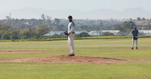 Diverse teammates pitching and fielding on baseball mound during daytime practice