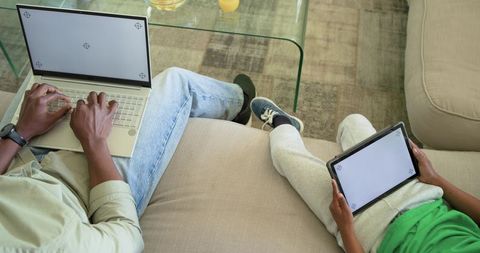 African American father and child using laptop and tablet while relaxing on couch