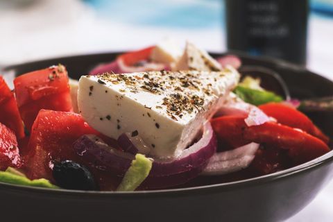 Creamy feta wedge topping fresh tomato red onion olive greek salad close-up