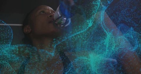 Mid-adult woman tilting sports bottle and drinking during gym workout with teal particle overlay