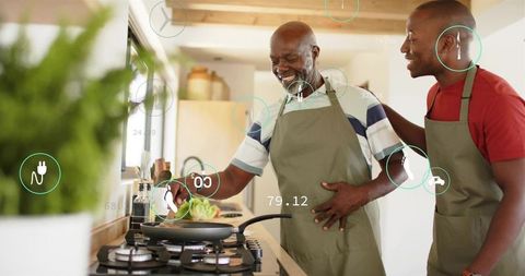 Father and son cooking together in bright modern kitchen wearing olive aprons, smiling