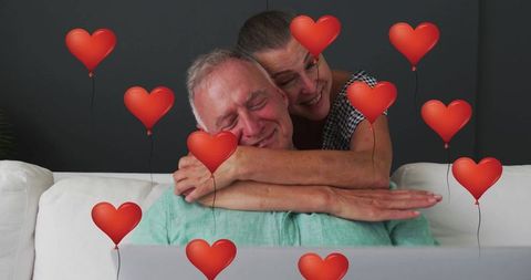 Senior Couple Embracing With Heart Balloons and Laptop