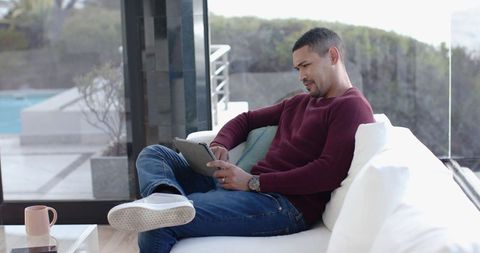 Man Relaxing on Modern Sofa with Tablet Near Large Windows