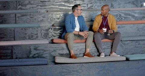 Diverse coworkers chatting on tiered seating in modern office lounge with cushions