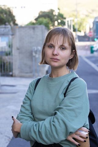 Young woman standing on urban street holding takeaway coffee cup wearing backpack
