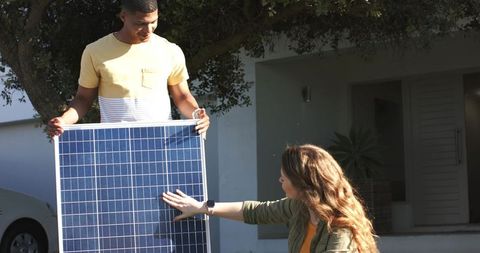 Diverse couple installing solar panel on driveway demonstrating renewable energy teamwork
