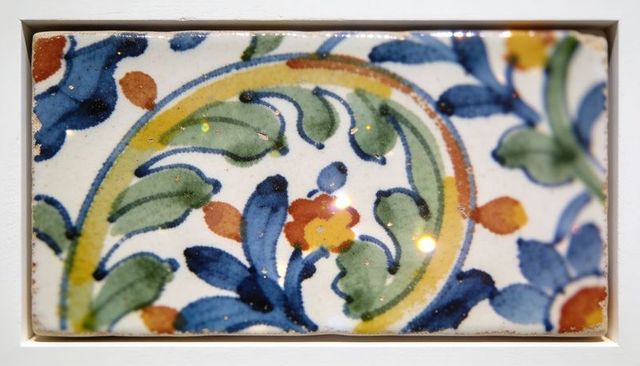 Hand-painted glazed ceramic tile featuring floral motif in white frame showing wear, blue green yell