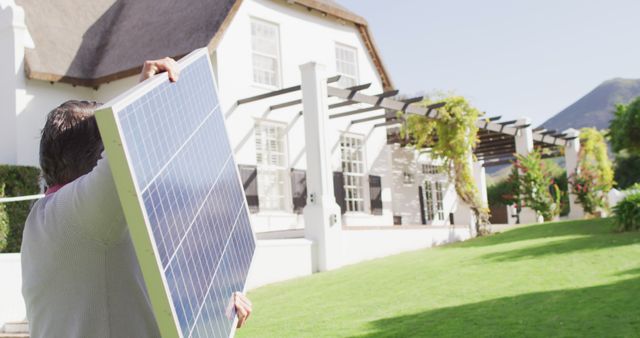 Image of caucasian man carrying solar panel in sunny garden. Domestic life, energy, reocurces and solar power concept digitally generated image.