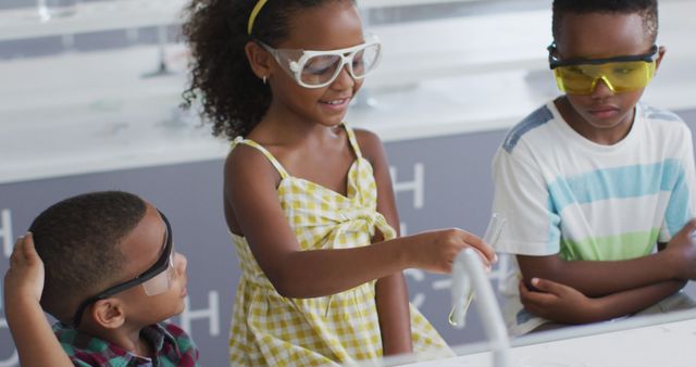 Three children in a science class wear safety glasses while performing a chemistry experiment. With focused expressions, they engage with test tubes and lab equipment, showcasing teamwork and curiosity. Ideal for educational content, school brochures, promoting STEM programs, and illustrating child learning activities.