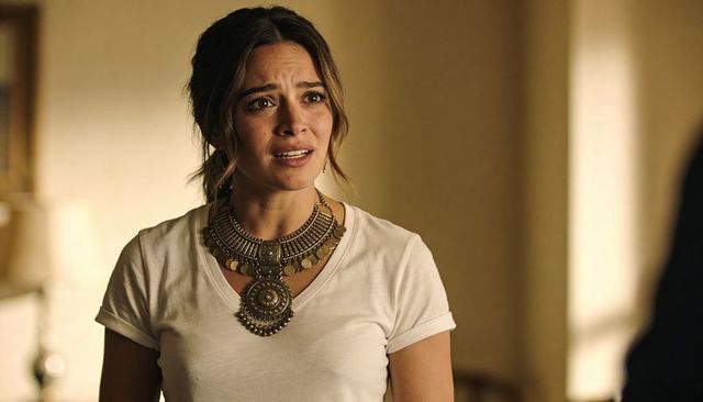 Young woman expressing concern wearing ornate statement necklace and white tee in warm room