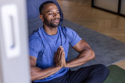 Mature african man meditating at home on yoga mat practicing mindfulness and prayer, calm focus