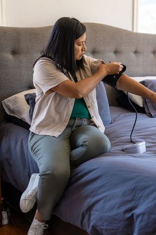 Asian woman measuring blood pressure on bed using automatic arm cuff for home care