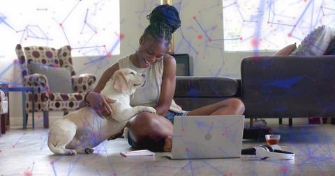 Smiling woman petting labrador while using laptop on living room floor, cozy home scene