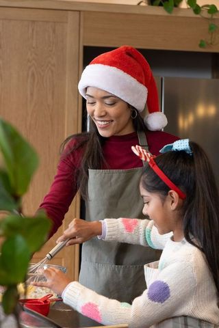 Asian mother and daughter mixing holiday batter in kitchen wearing santa hat and apron