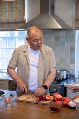 Senior asian man chopping red onion on wooden cutting board in cozy home kitchen