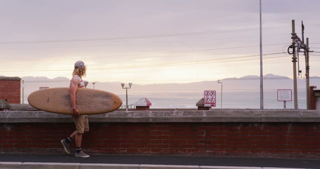 Caucasian male surfer walking in street carrying surfboard at sunset, unaltered, with copy space. Surfing, sports, hobbies and free time.