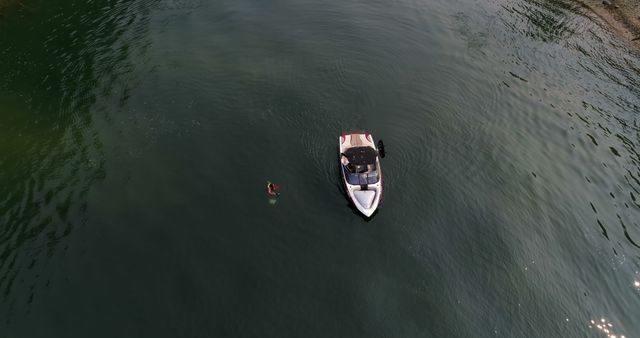 Motorboat on calm water with swimmer nearby viewed from above, ideal for depicting outdoor lifestyle, recreational boating, or summer activities. Suitable for travel magazines, websites promoting outdoor adventures, and tourism advertisements.