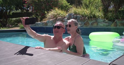 Senior couple enjoying sunny backyard pool selfie showing togetherness and summer leisure