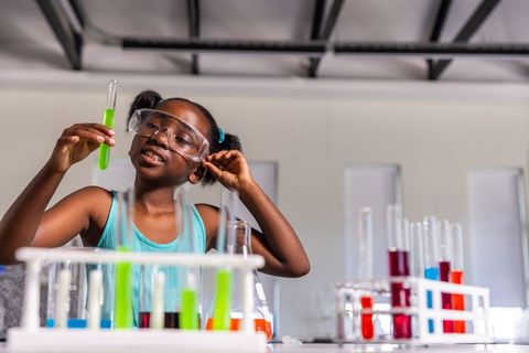 African american girl wearing safety goggles conducting colorful chemistry experiment in school lab