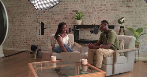 African co-hosts recording relaxed home podcast with laptop, studio microphones, softbox