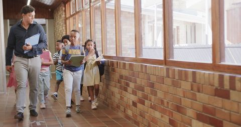 Diverse Teacher Guiding Young Students Down School Hallway
