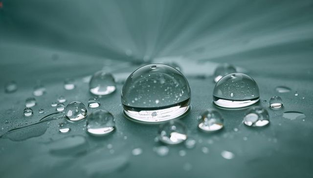Macro water droplet resting on green leaf with bokeh reflections and dew beads