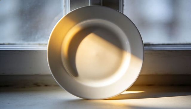 White ceramic plate catching warm sunbeam on windowsill, minimal still life