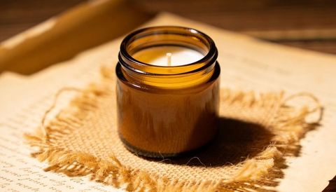 Amber glass jar candle on burlap and aged paper rustic vintage still life with warm light