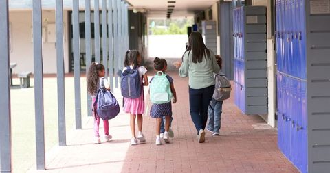 Teacher Leading Young Students in School Hallway