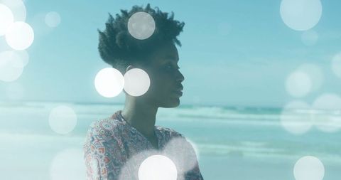Woman in paisley blouse gazing at ocean with bokeh lights