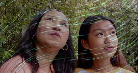 Two Women Gazing Upward in Sunlit Garden Wearing Hoop Earrings and Striped Top